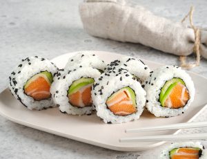 A set of fresh sushi rolls with salmon, avocado and black sesame seeds served on a plate with chopsticks. Japanese sushi uramaki or California roll